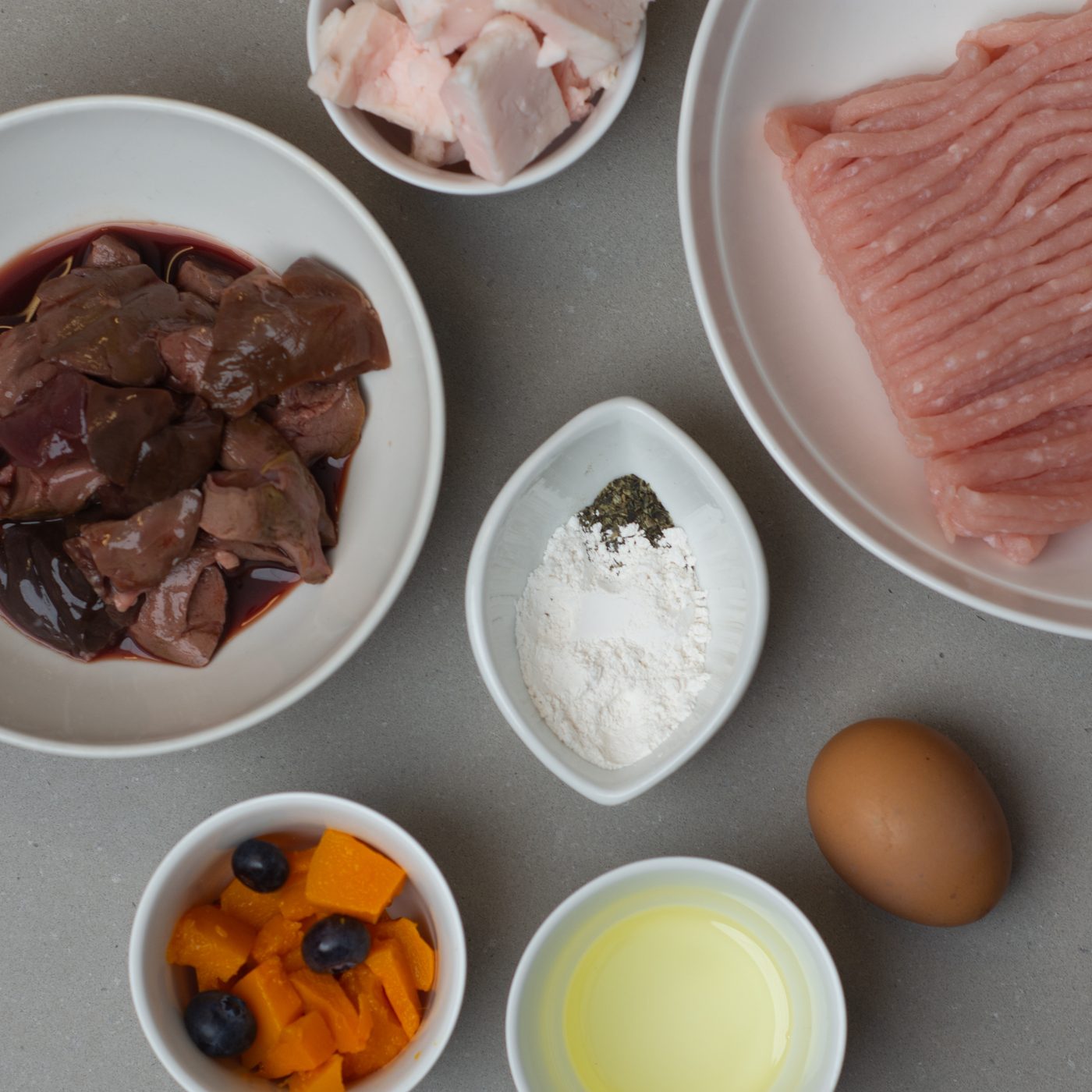 The building blocks of a balanced French Bulldog meal: minced turkey, liver, fat, egg, pumpkin, blueberries and supplements laid out in bowls